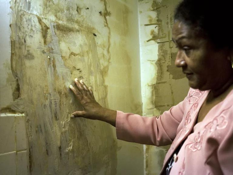 A woman looks at a wall with water damage and mold visible