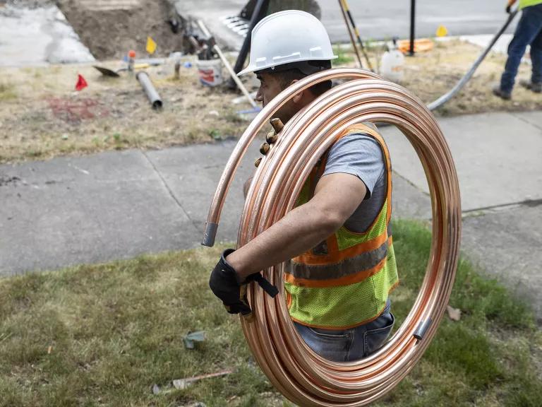 A worker carrying a coil of copper piping during a lead service line replacement