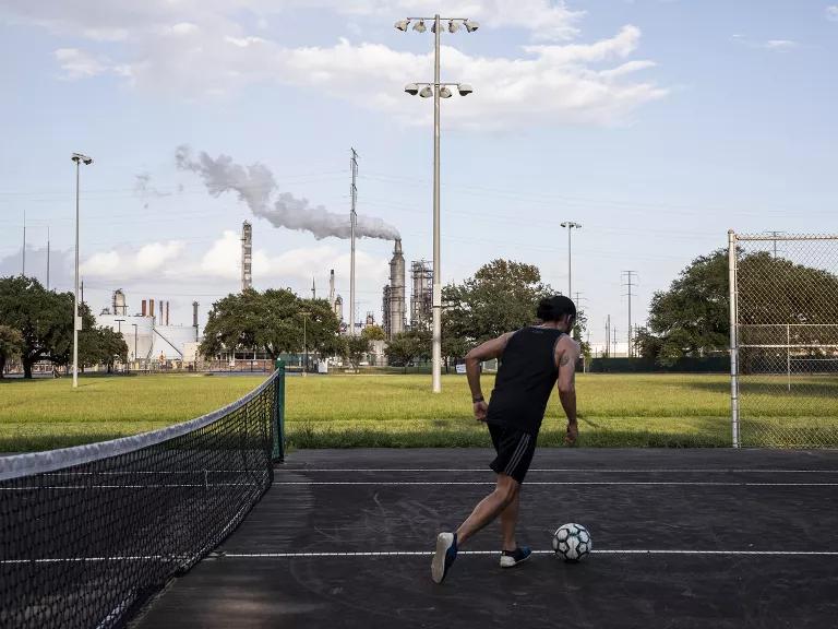 A soccer player practices at a park in Houston as emissions rise from a nearby oil refinery.
