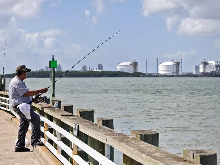 A man fishing from a pier near a liquefied natural gas facility in Louisiana