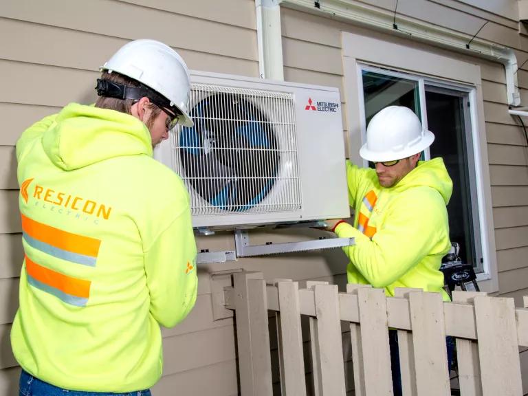 Image of two HVAC technicians installing a Mitsubishi heat pump