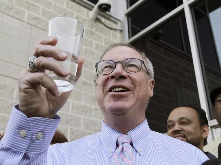 A person in glasses holding up a glass of water