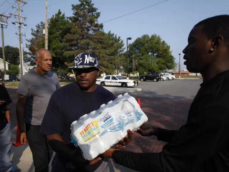 A person in a black shirt and a baseball cap holding a case of bottled water
