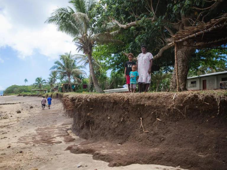 A woman and two of her grandchildren stand on the eroded coastline of Wiana Village on Emao Island, Vanuatu