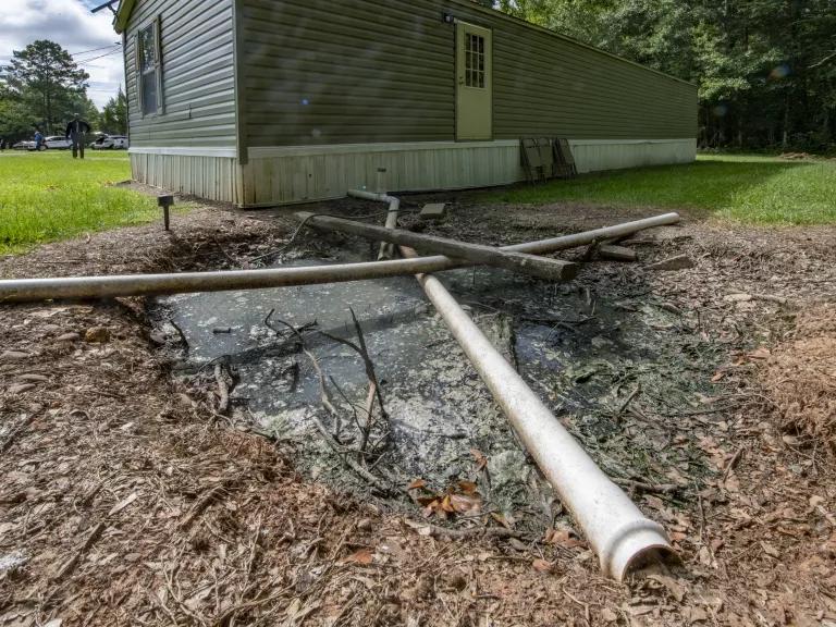 A pipe runs from the foundation of a house into a ditch in the backyard