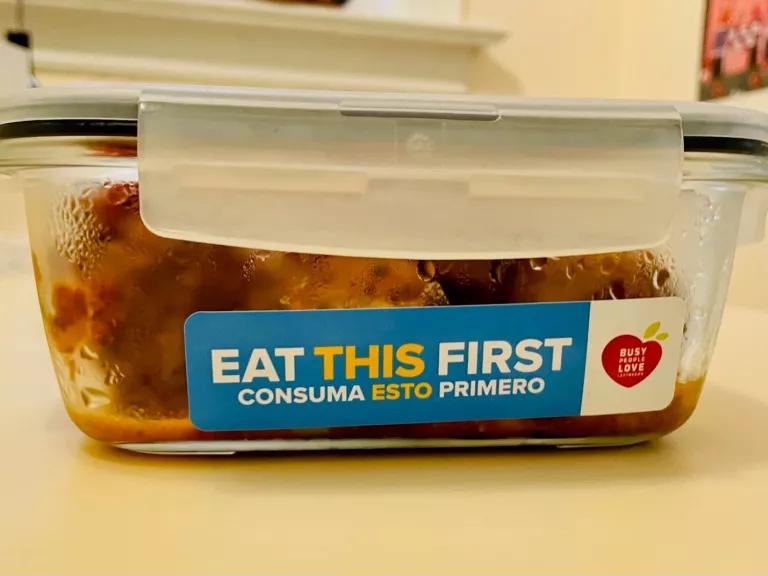 A covered glass food container with a sticker on the side that reads "Eat This First"
