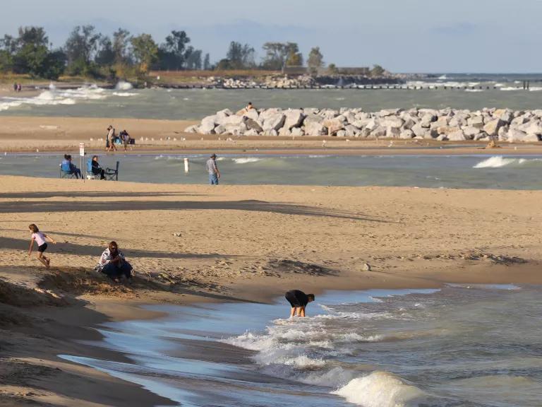 A wide angle view of a young Caucasian boy playing in low tide at Illinois Beach State Park. Breakwater structures made of large rocks and other beachgoers are visible in the background.