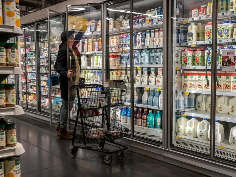 A Caucasian man opening the door of a commercial sized refrigerator filled with milk products at a supermarket