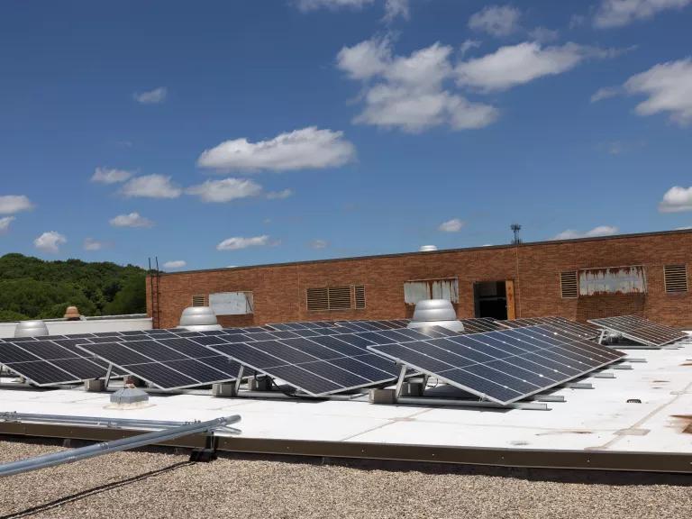 An array of solar panels with a red brick building in the background