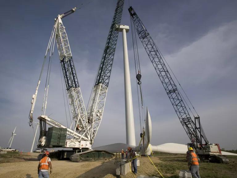 A wind turbine surrounded by two cranes and workers around them