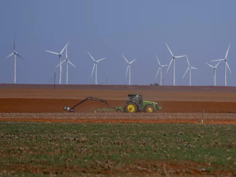 Wind turbines are visible as a farmer plows a cotton field in Lamesa, Texas, on February 26, 2025.