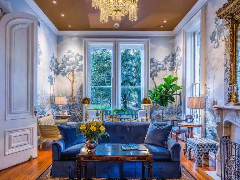 A room with a blue couch and floor to ceiling windows in the back
