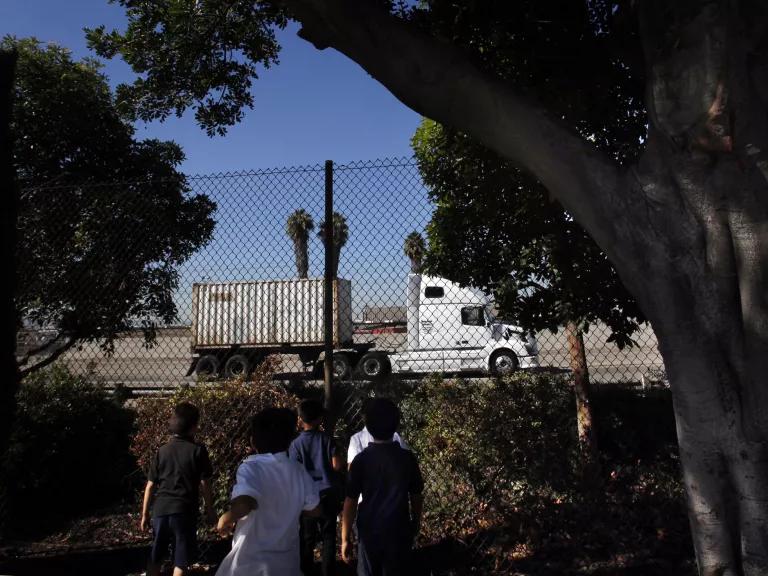 Children watch a semi-trailer truck passing on the 103 freeway next to Hudson Elementary School as they have recess on the playground on October 31, 2013.  Long Beach city leaders are considering a proposal to shut down part of the busy road to make green space.