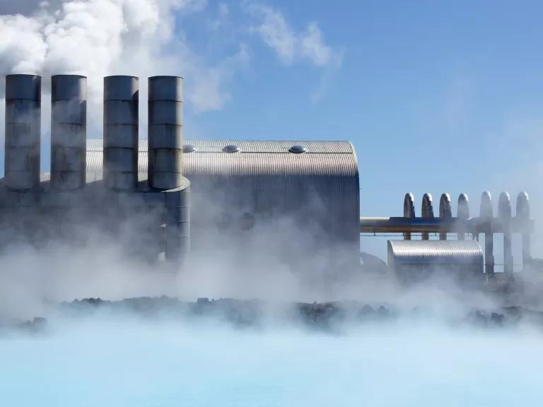 Steam rises off blue water in front of a power plant with four stacks