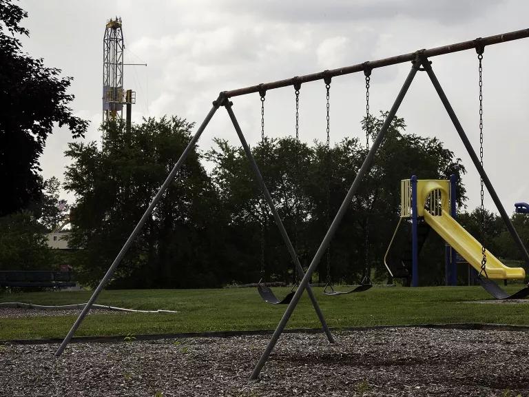 An empty playground with trees behind it and large oil rig standing in the background