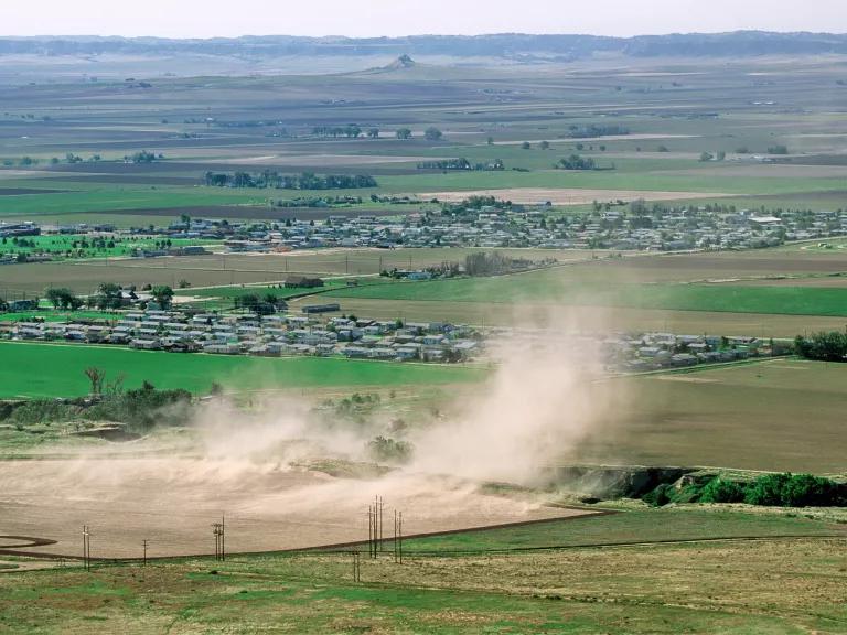 Clouds of dust rise up from a patch of brown dirt surrounded by greener fields.