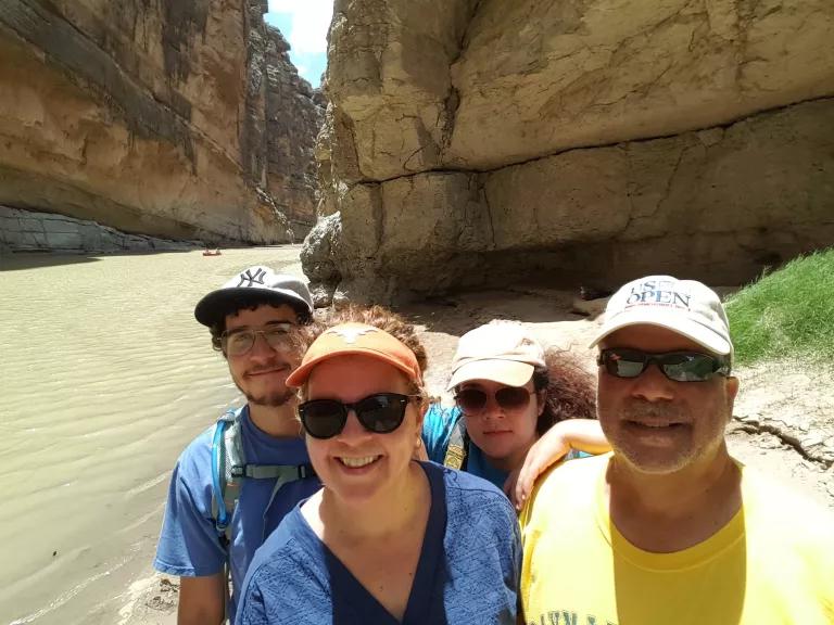 Four people on the bank of a narrow river with steep cliffs on either side