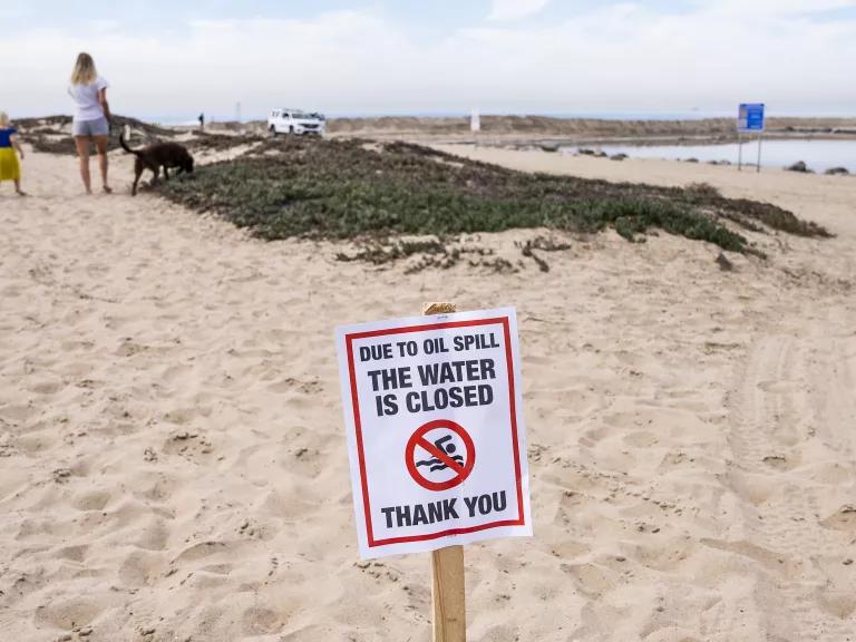 A sign posted in the sand on a beach reads "Due to the oil spill the water is closed. Thank you."