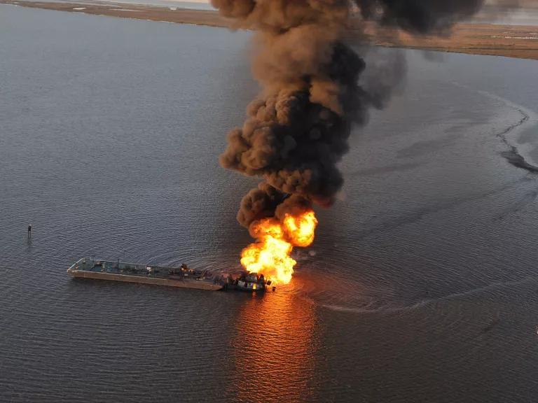 Flames and black smoke rise from a pipeline in the middle of a body of water