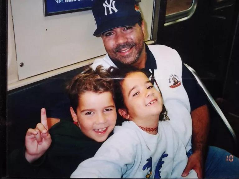 A man wearing a Yankees cap and two children in a subway car