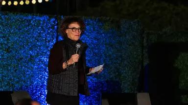 NRDC Board Chair Kathleen Welch standing in front of a blue back holding a microphone