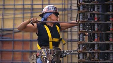 A worker bending rebar while hanging from a harness on a construction site.