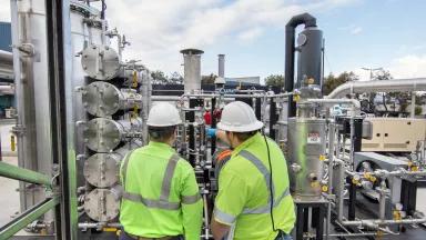 Two workers inspect pipes at a dry anaerobic digestion (AD) solid waste processing facility which converts food and green organic waste into biogenic compressed natural gas (CNG) and soil amendments in San Francisco, California.