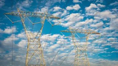 High voltage power lines and pylons against a cloud-filled blue sky