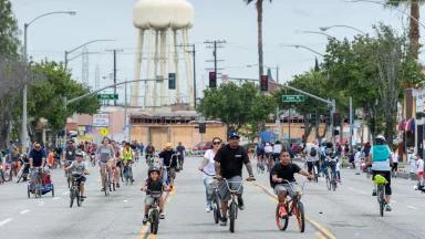 Adults and children riding bicycles in all lanes of a wide Los Angeles street, with no cars in sight