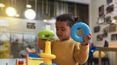 A toddler playing with a plastic stacking toy in a classroom.