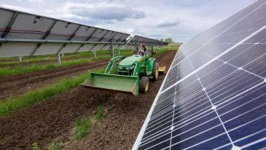 A worker uses a tractor to till the soil between solar panel arrays at a community solar farm in Colorado.