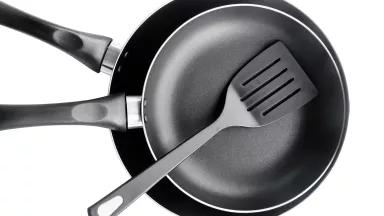 Teflon-coated non-stick frying pans and a plastic spatula, isolated on a white background.