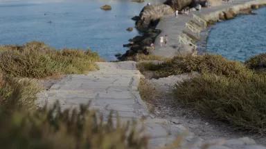 People walk along a narrow, rocky pathway with bodies of water on both sides