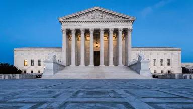 A wide-angle view of the exterior of the U.S. Supreme Court, lit up at dusk
