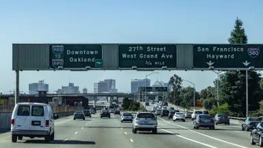 Cars drive toward the downtown Oakland skyline on a highway in the foreground (California's I-980)