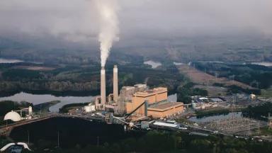 An aerial view of emissions rising from a coal-fired power plant located next to a lake