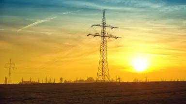 Photo of a high-voltage electricity transmission towers silhouetted against a sunset or sunrise.