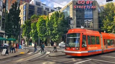 An orange streetcar appears to gluide along the street. A sign hung on a nearby building reads "GO BY STREETCAR."