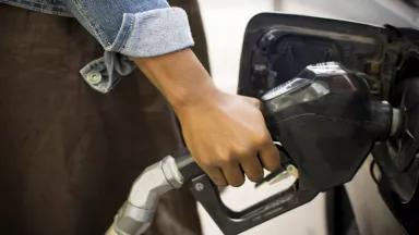A woman filling a car's gas tank with a gas pump.