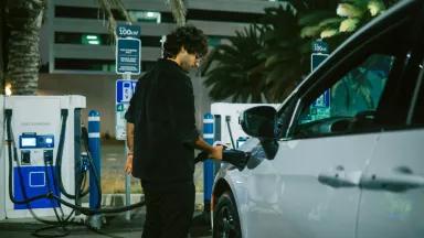 A man charging his electric car at a charging station in Santa Monica, Los Angeles, California, in the evening.