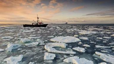 A fishing boat moves through the Bering Sea, a field of sea ice in the foreground