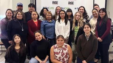 A group portrait of people in front of a sign with the logos RISE and SciCAN