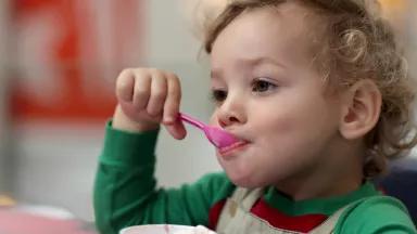 A toddler eats ice cream using a plastic spoon.