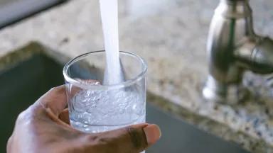 A woman filling a water glass at her kitchen sink.