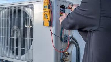 A technician using a multimeter to test voltage on a mini-split heating and cooling system.