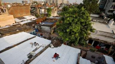 An aerial view of two painters creating ‘cool roofs’ by applying solar reflective paint to homes in a slum neighborhood of Ahmedabad, India