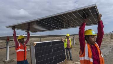 Workers carry a solar panel at the under-construction Adani Green Energy Limited's Renewable Energy Park in the salt desert of Karim Shahi village, Gujarat, India, on September 21, 2023.