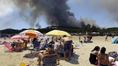 People sunbathing on the beach in Lavandou, French Riviera, as plumes of smoke rise in the air from burning wildfires in the forest of La Londe-les-Maures, France on Wednesday, July 26, 2017.