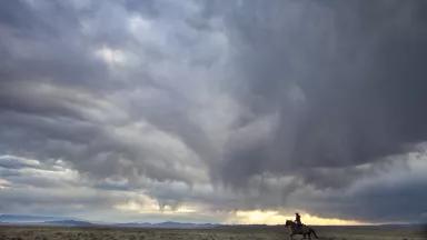 A lone rider on horseback on a vast plain under cloudy skies