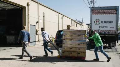 Workers pull a pallet of crates from a truck to a warehouse